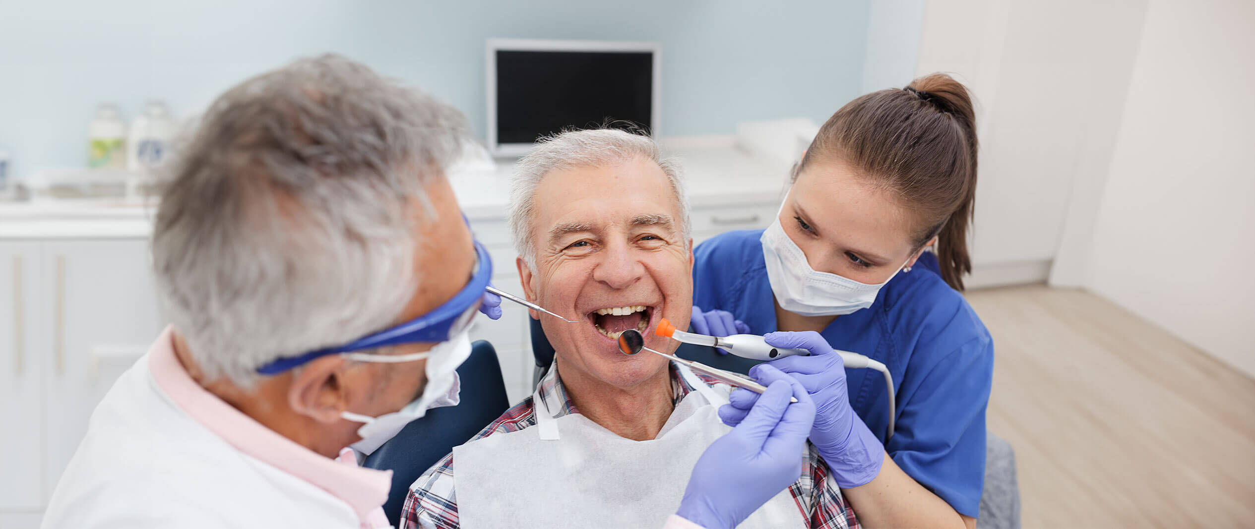 This is a playful image of dental staff providing periodontics treatment to a smiling man.